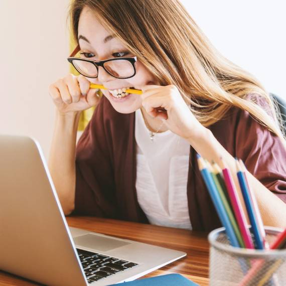 young asian woman at her laptop chewing a pencil